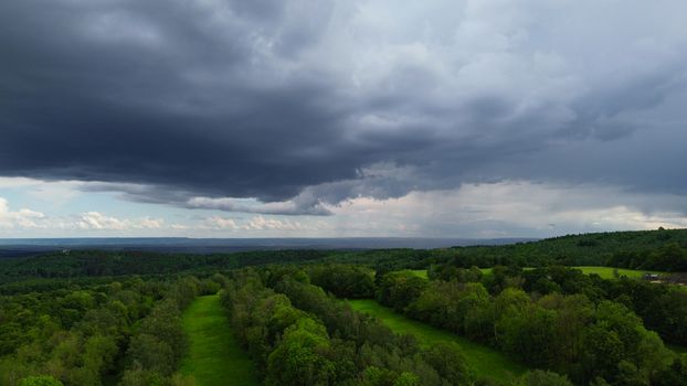 Aerial view of lush green forest under dark storm clouds in Blatno, Česko, capturing a dramatic summer landscape.