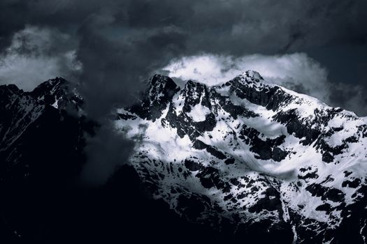 Snowcapped peaks of majestic mountains enveloped by dramatic clouds, showcasing winter's allure.
