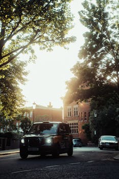 LEVC taxi navigating a sunlit street in a London neighborhood, surrounded by trees and architecture.