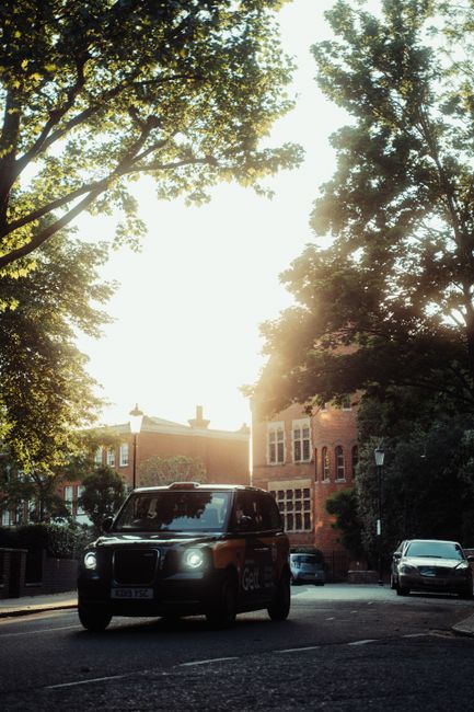 LEVC taxi navigating a sunlit street in a London neighborhood, surrounded by trees and architecture.