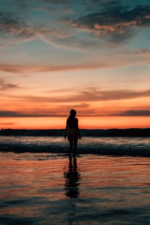 Free A solitary figure stands in ocean waves at sunset, captured in Máncora, Peru. Stock Photo