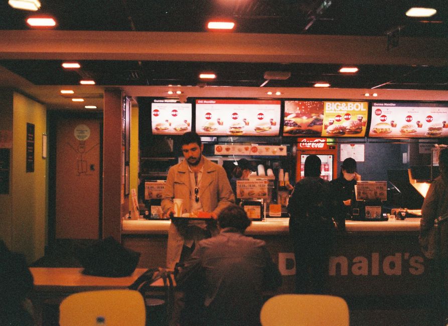 A retro-themed fast food restaurant scene with people ordering and dining inside. A retro-themed fast food restaurant scene with people ordering and dining inside.