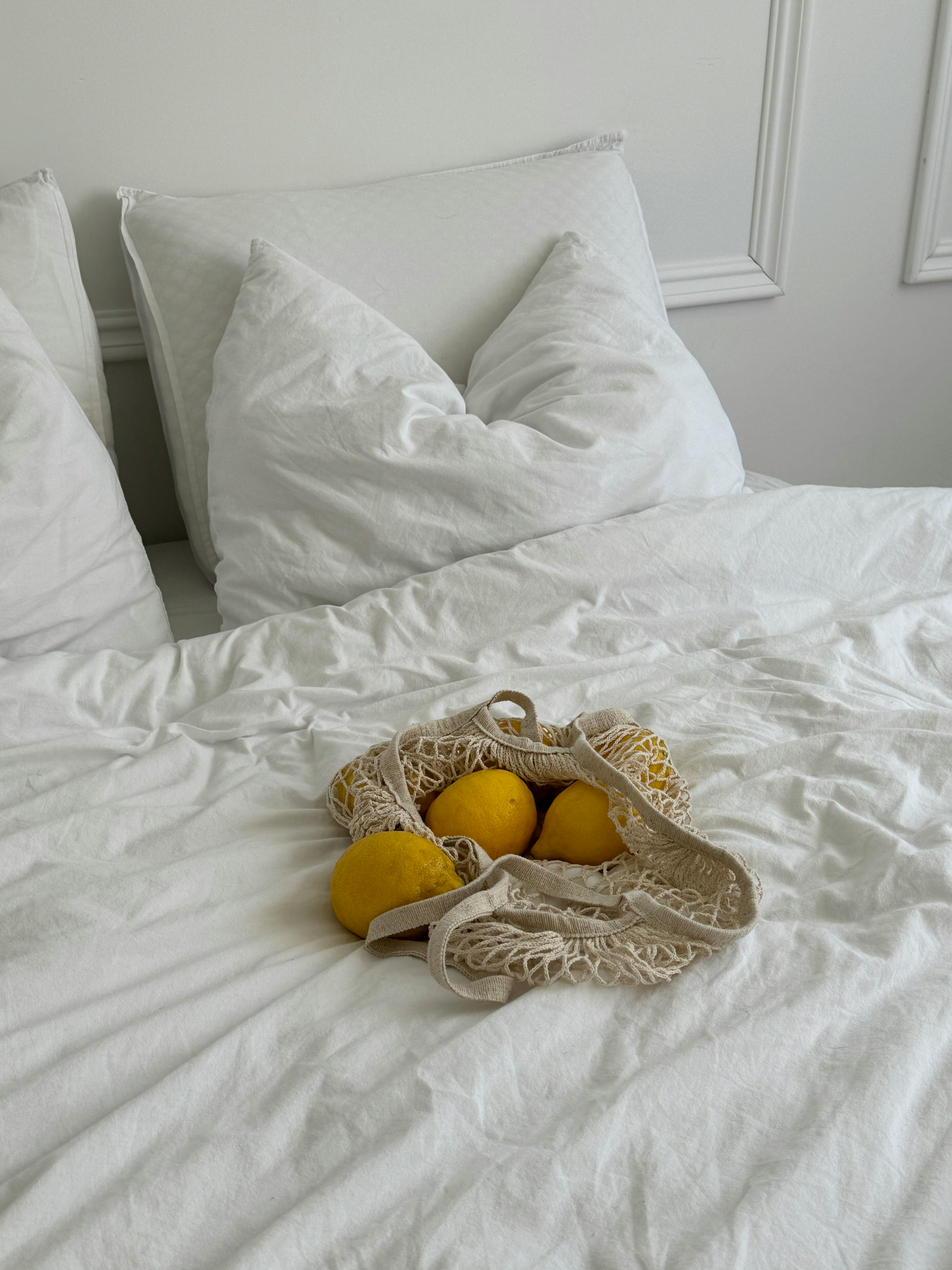 Cozy white bedding with bright lemons in a net bag, evoking freshness and tranquility.