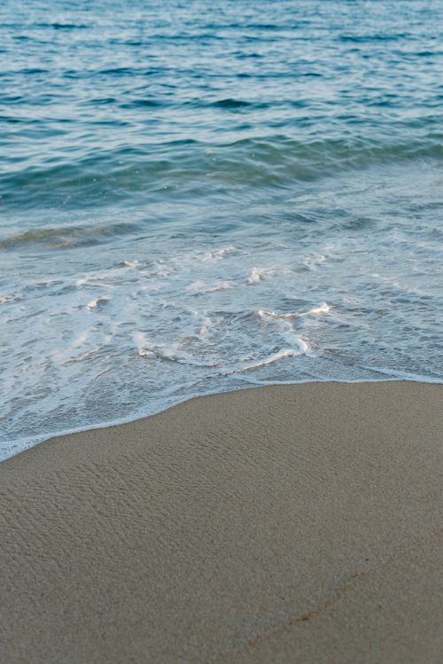 Free Serene beach scene capturing gentle waves meeting the sandy shore under a tranquil sky. Stock Photo