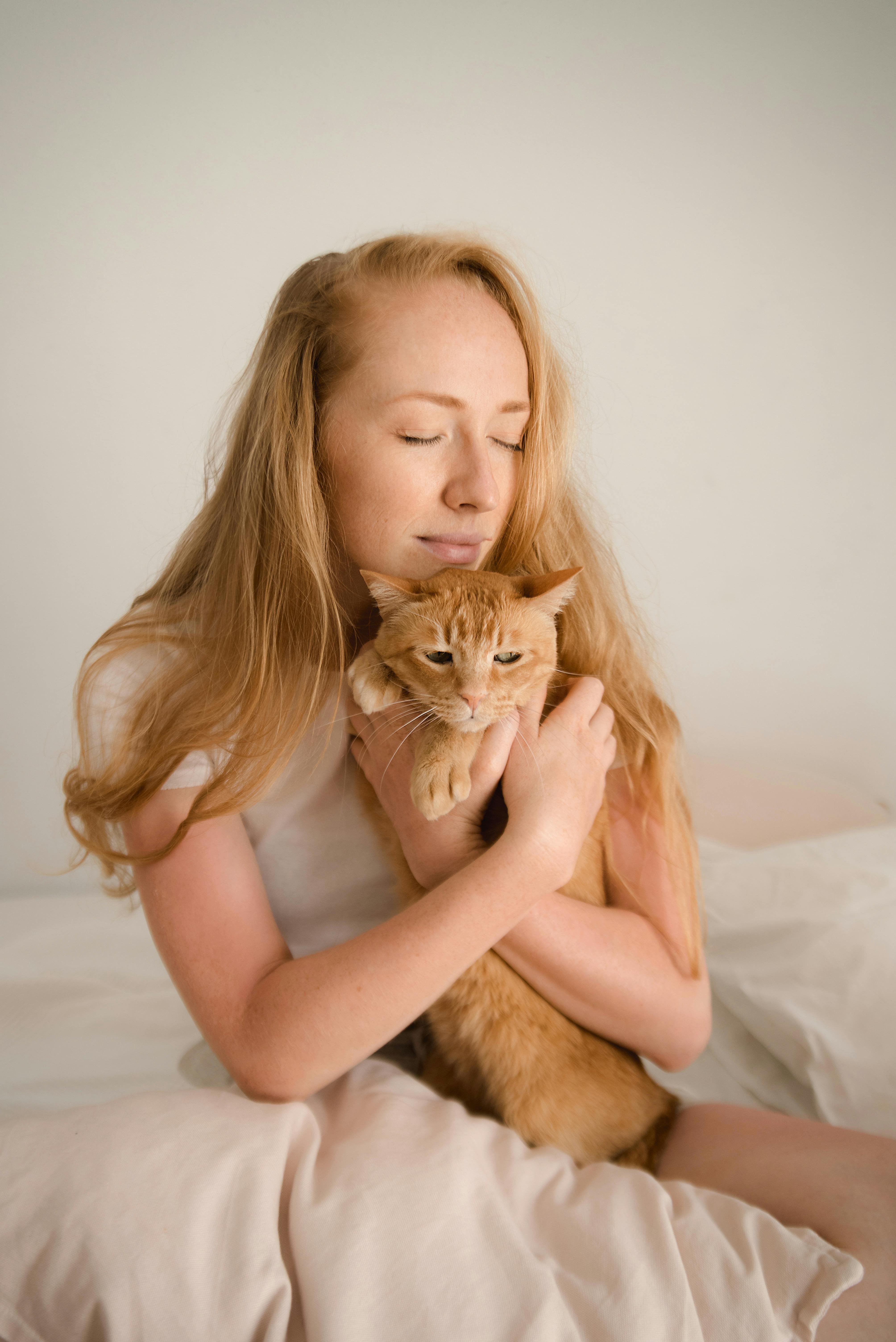 A woman lovingly hugs an orange cat while sitting indoors, with a sense of tranquility.