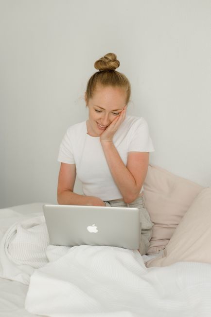A woman sitting in bed, smiling while using a laptop. Perfect for lifestyle and technology themes.