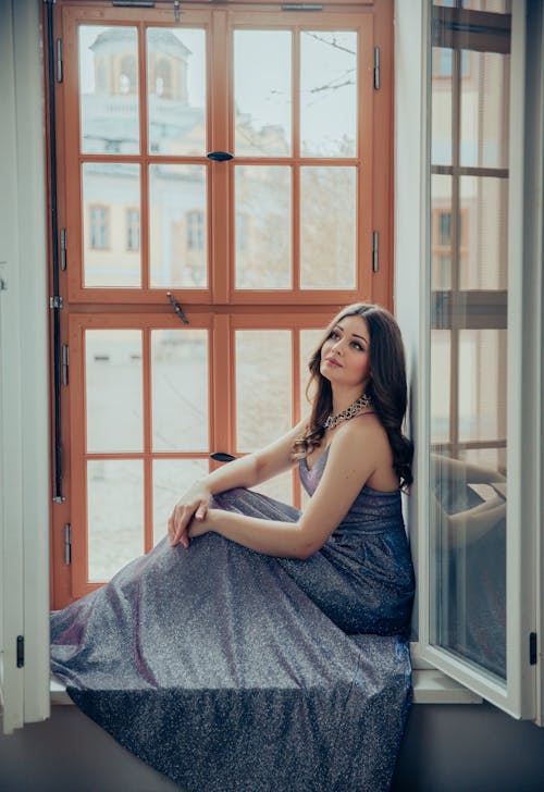 A woman in a long dress sitting in a window
