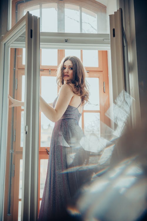 A woman in a long dress looking out of a window