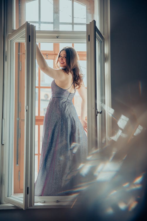 A woman in a long dress standing in an open window