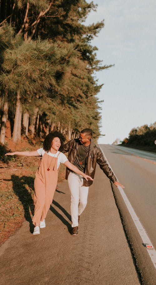 Free Smiling Couple Walking with Arms Stretched on Road Stock Photo