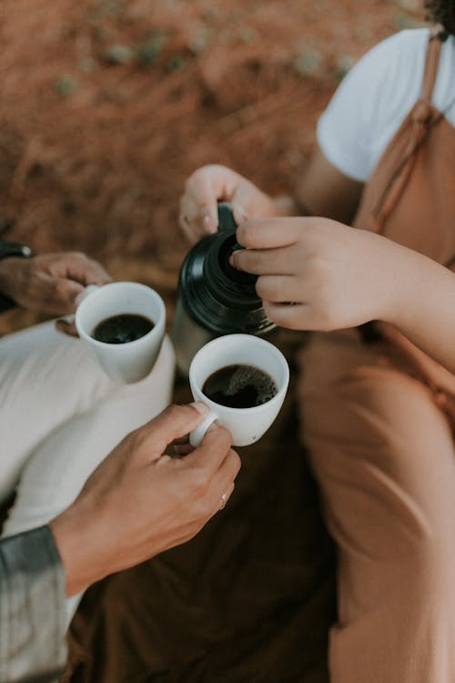 Two people holding coffee cups and sitting on a blanket