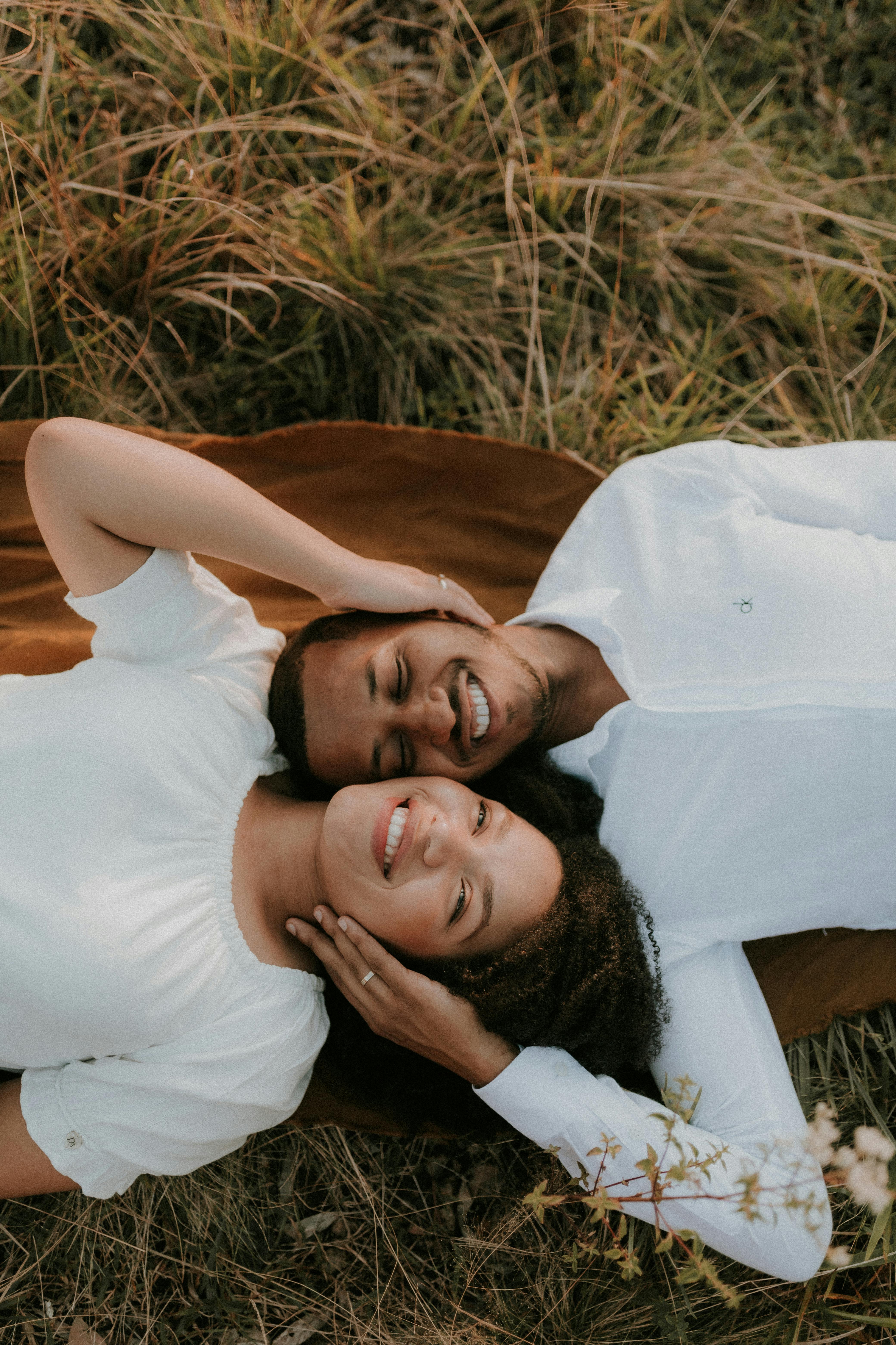 A loving couple in white clothing lying on grass, enjoying a moment together.