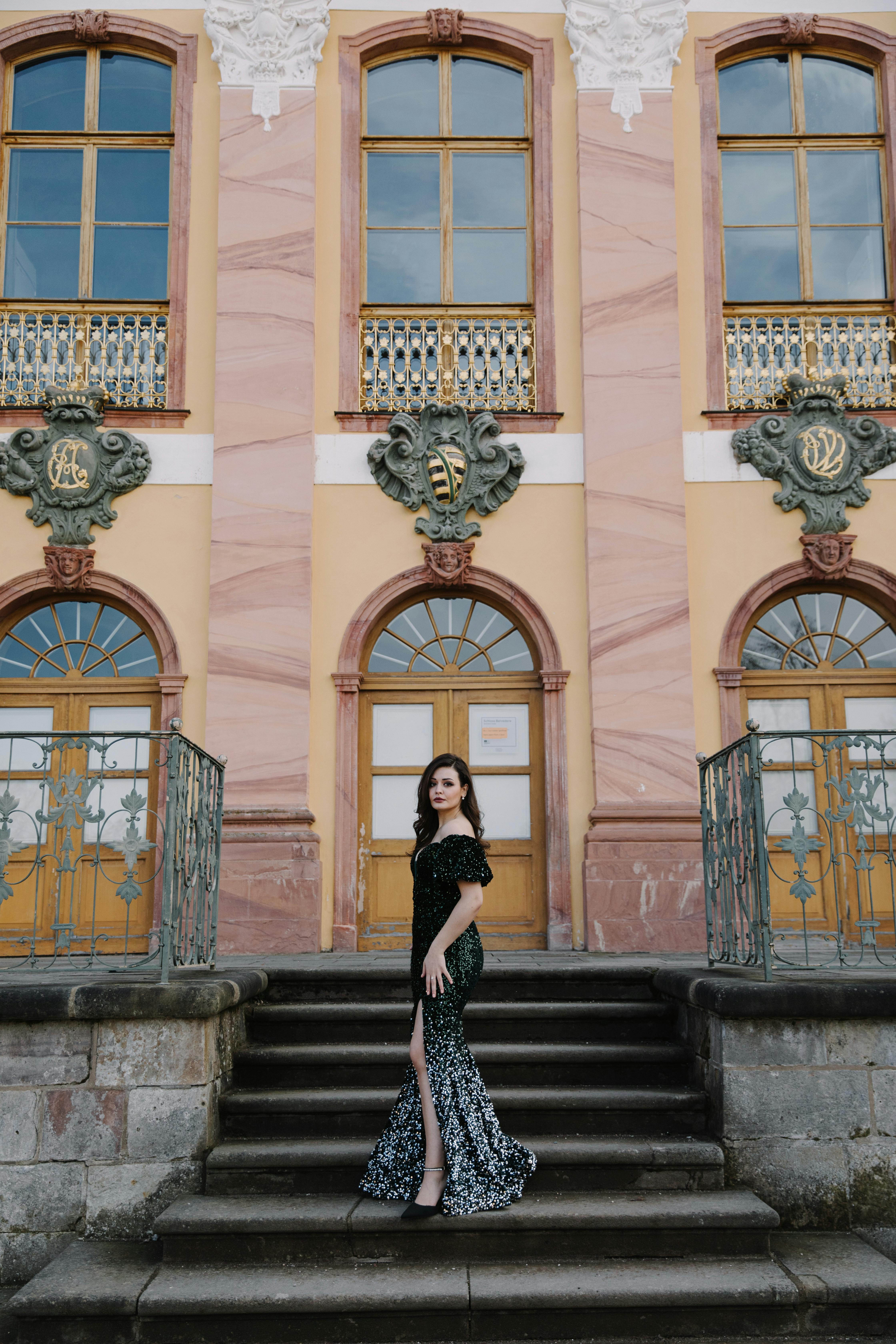 Woman in elegant dress posing on staircase in front of a historic building.