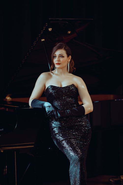 A woman in a black sequin dress posing next to a piano