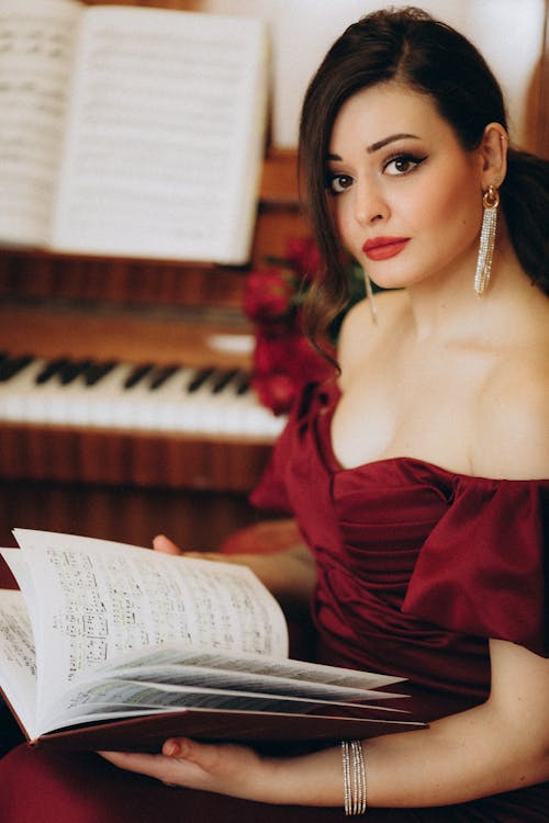 A woman in a red dress holding a book and playing the piano