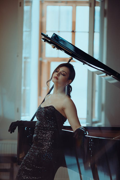 A woman in a black dress posing next to a grand piano
