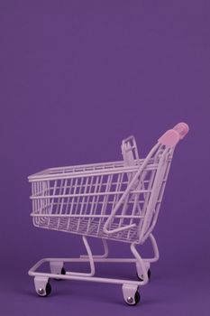 Minimalist image of a pink shopping cart on a purple background, featuring ample copy space.