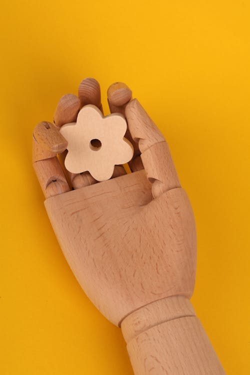 A wooden hand holding a flower on a yellow background