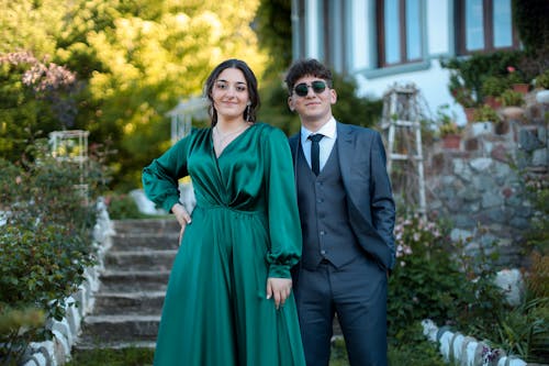 A man and woman in green dresses standing in front of a house