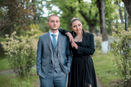 A man and woman in formal wear standing in a park