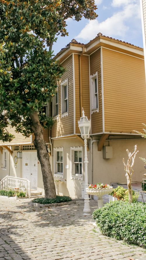 Free Idyllic two-story house with wooden facade, tree, and classic lamppost on a sunny day. Stock Photo