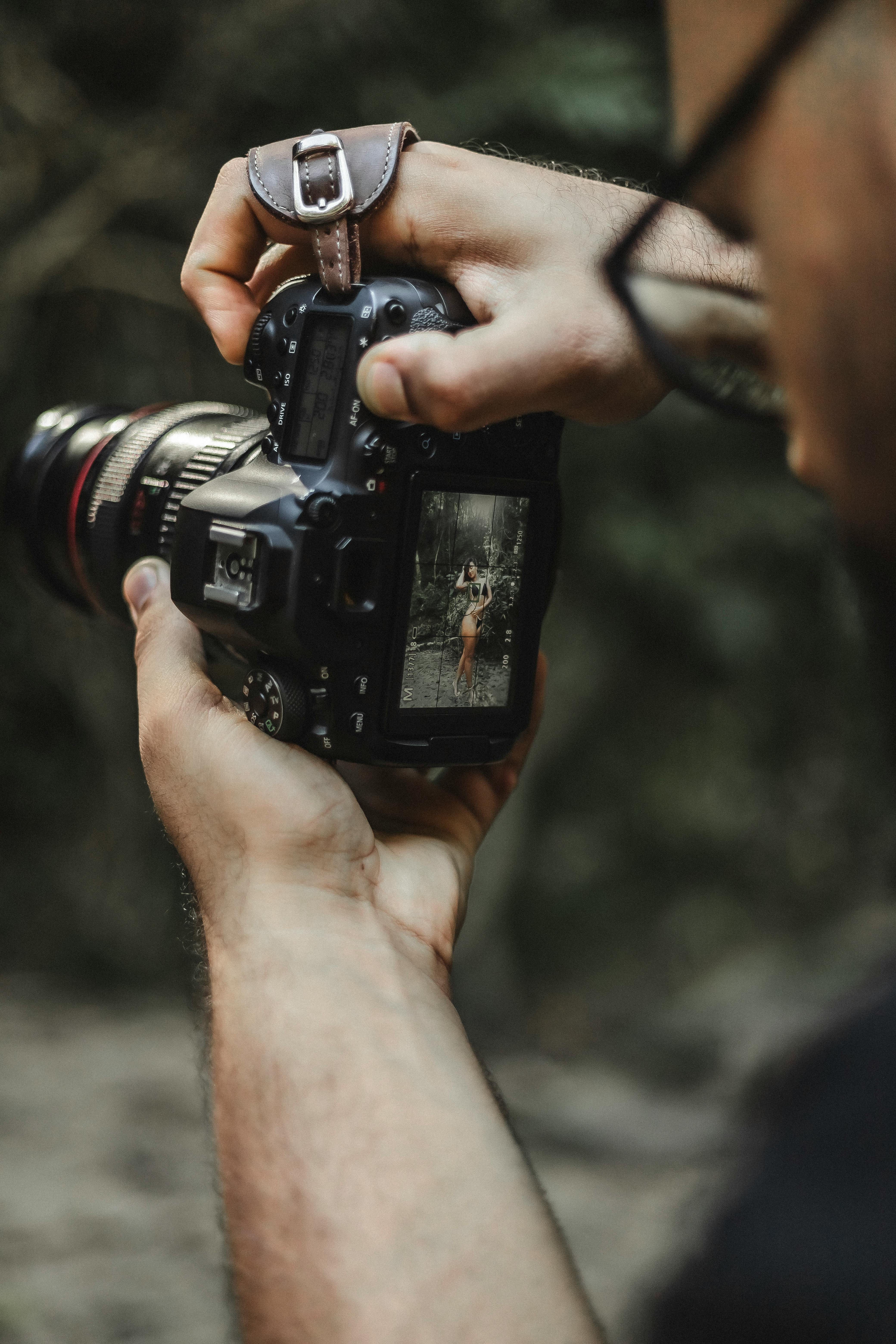 Free Photographer holding DSLR camera taking a picture of nature. Close-up view from behind. Stock Photo