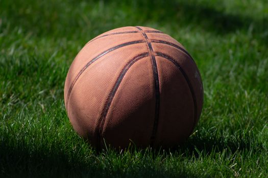 Close-up of a basketball resting on lush green grass, highlighting sports and recreation.