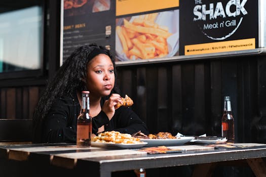 Young woman enjoying a chicken meal with drinks at a restaurant table.