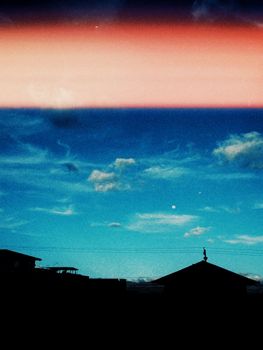 Silhouette of houses against a vibrant blue sky with clouds and a hint of sunset hues.