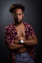 一位戴眼镜的非裔美国男子，身着花卉衬衫，在暗色背景前摆着姿势