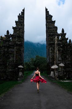 在印度尼西亚巴厘岛著名的汉达拉门，一名身穿红色连衣裙的女子在雾蒙蒙的群山中旋转