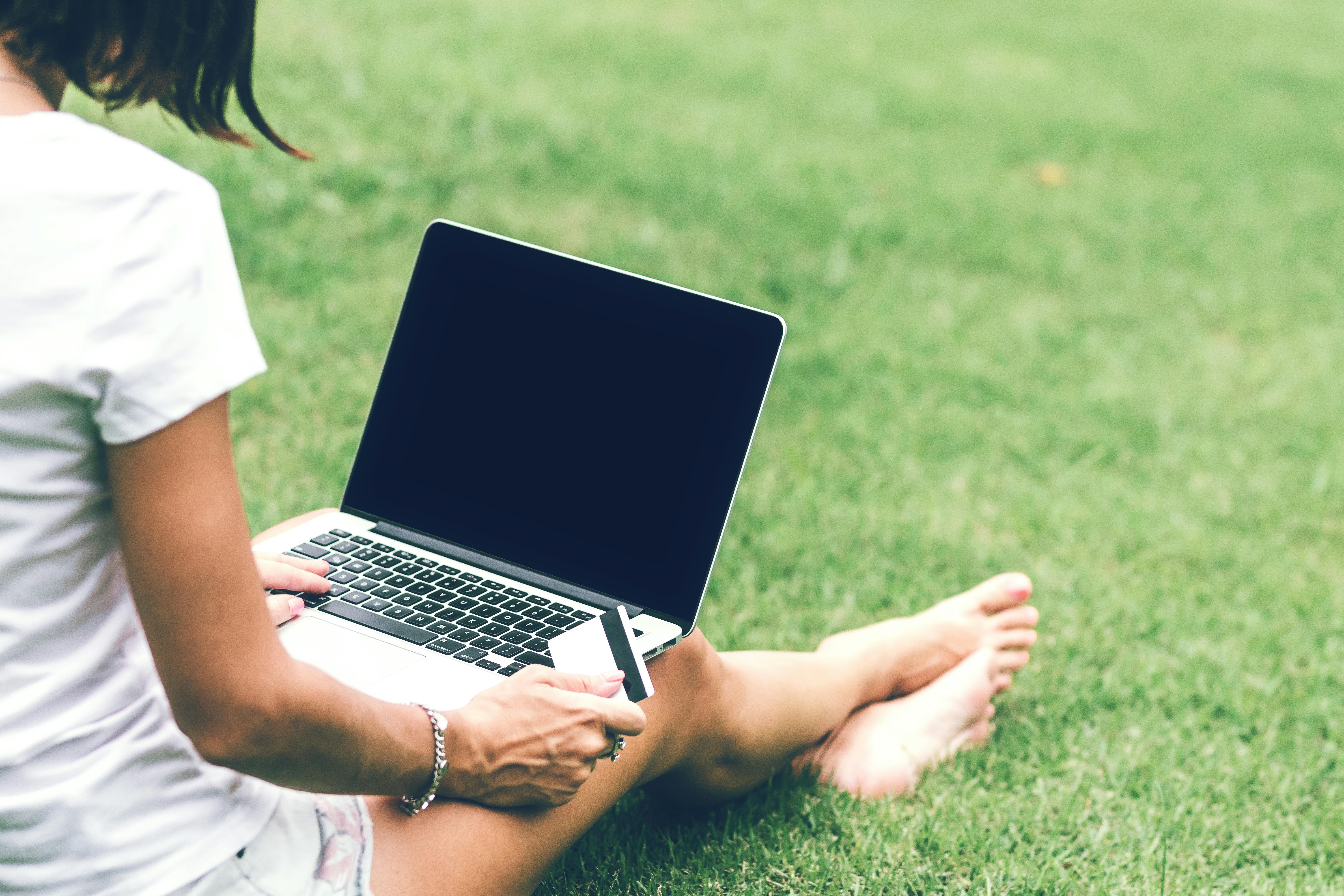 Photo of a Woman Sitting on Lawn Grass Holding Card with Mac book air on Laps