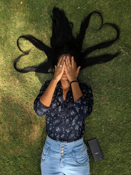 Foto Der Frau, Die Auf Grasfeld Liegt, Das Ihr Gesicht Mit Ihren Händen Bedeckt