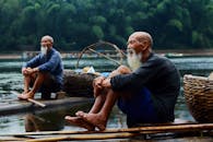 两位老人坐在河边的竹排上，悠闲地垂钓，享受着宁静的时光