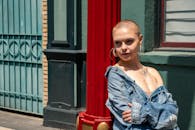 一位前卫风格、带有纹身的年轻女子穿着牛仔夹克在户外摆姿势，明亮的日光凸显了她的时尚感