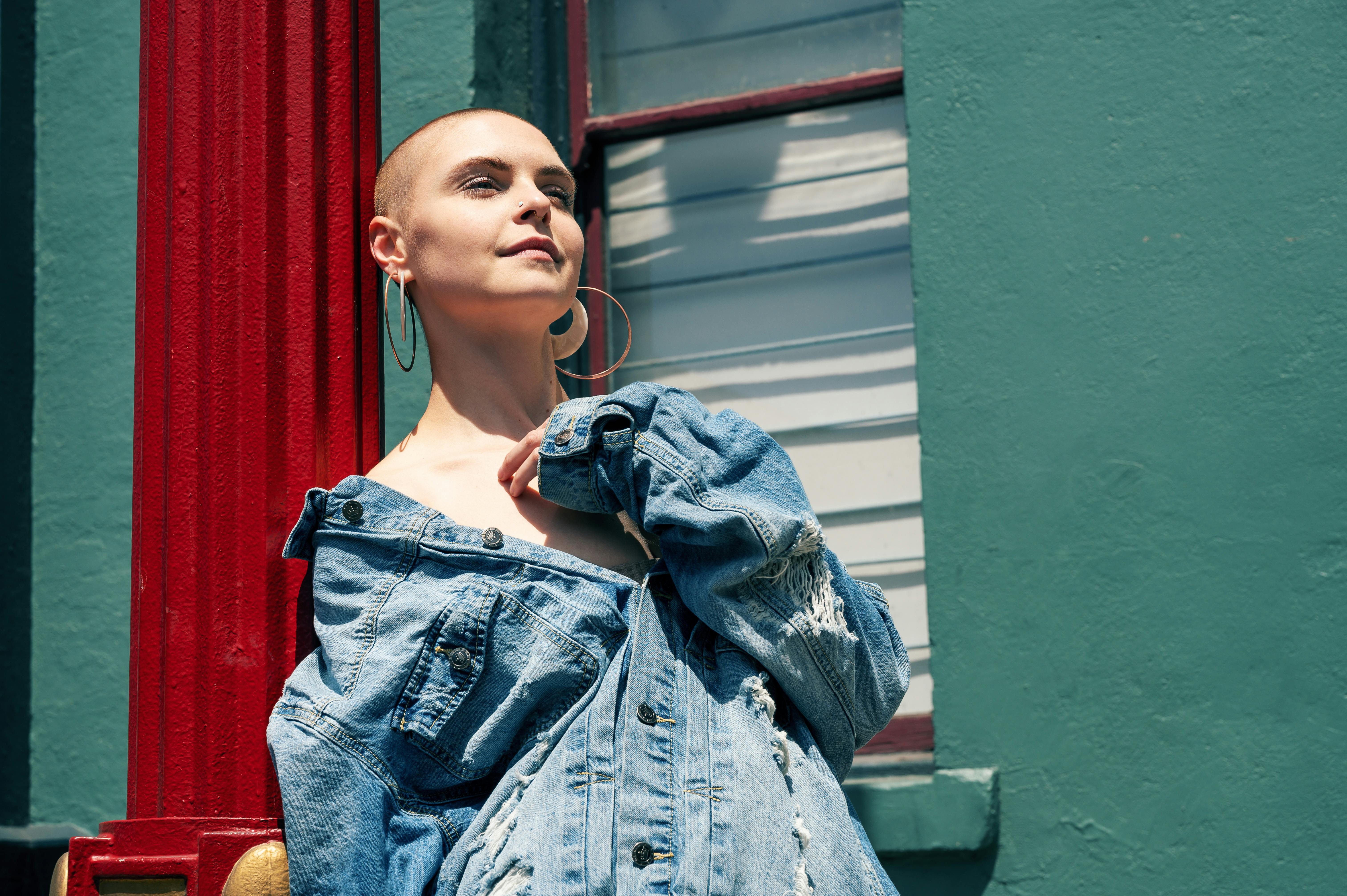 Stylish woman with short hair posing in a denim jacket under sunlight.