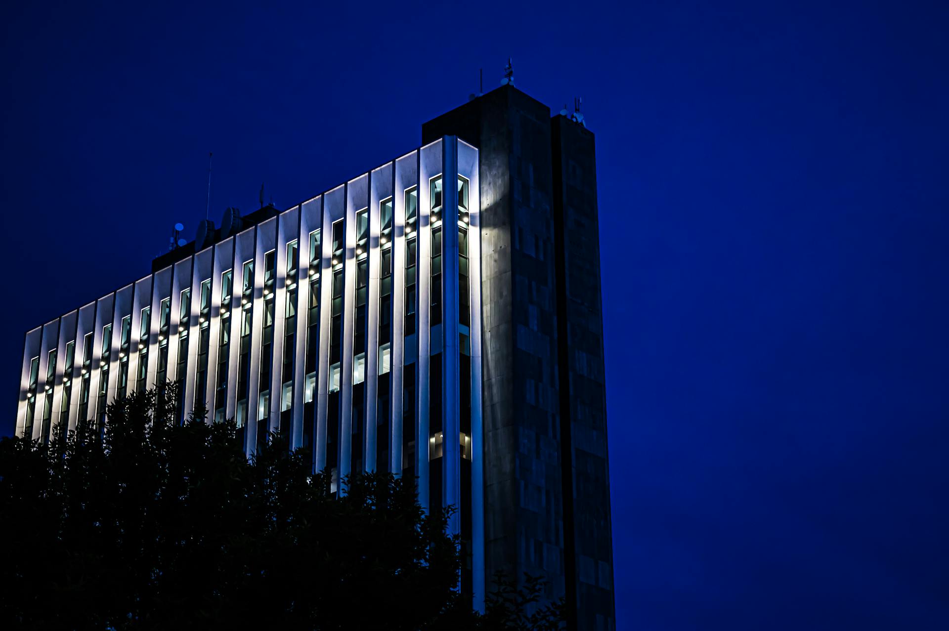 A contemporary high-rise office building illuminated against a dark evening sky.