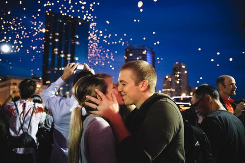 Free A couple shares a kiss during a lively night celebration with floating lights in the cityscape. Stock Photo