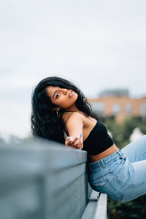 Photo of Woman in Black Crop Top and Blue Jeans Leaning Backwards on Metal Railing