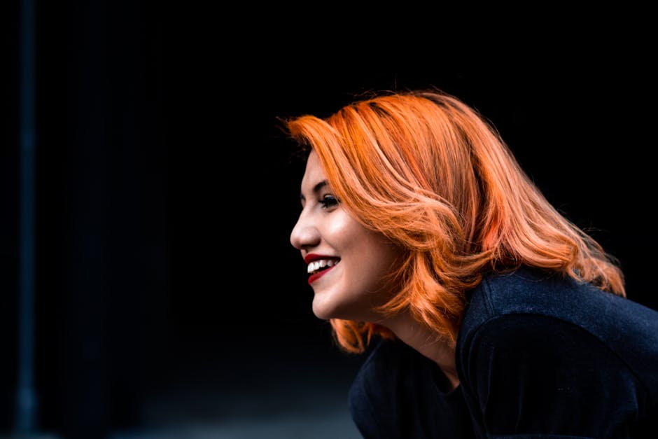 Portrait of a smiling redhead woman with vibrant hair against a dark background.