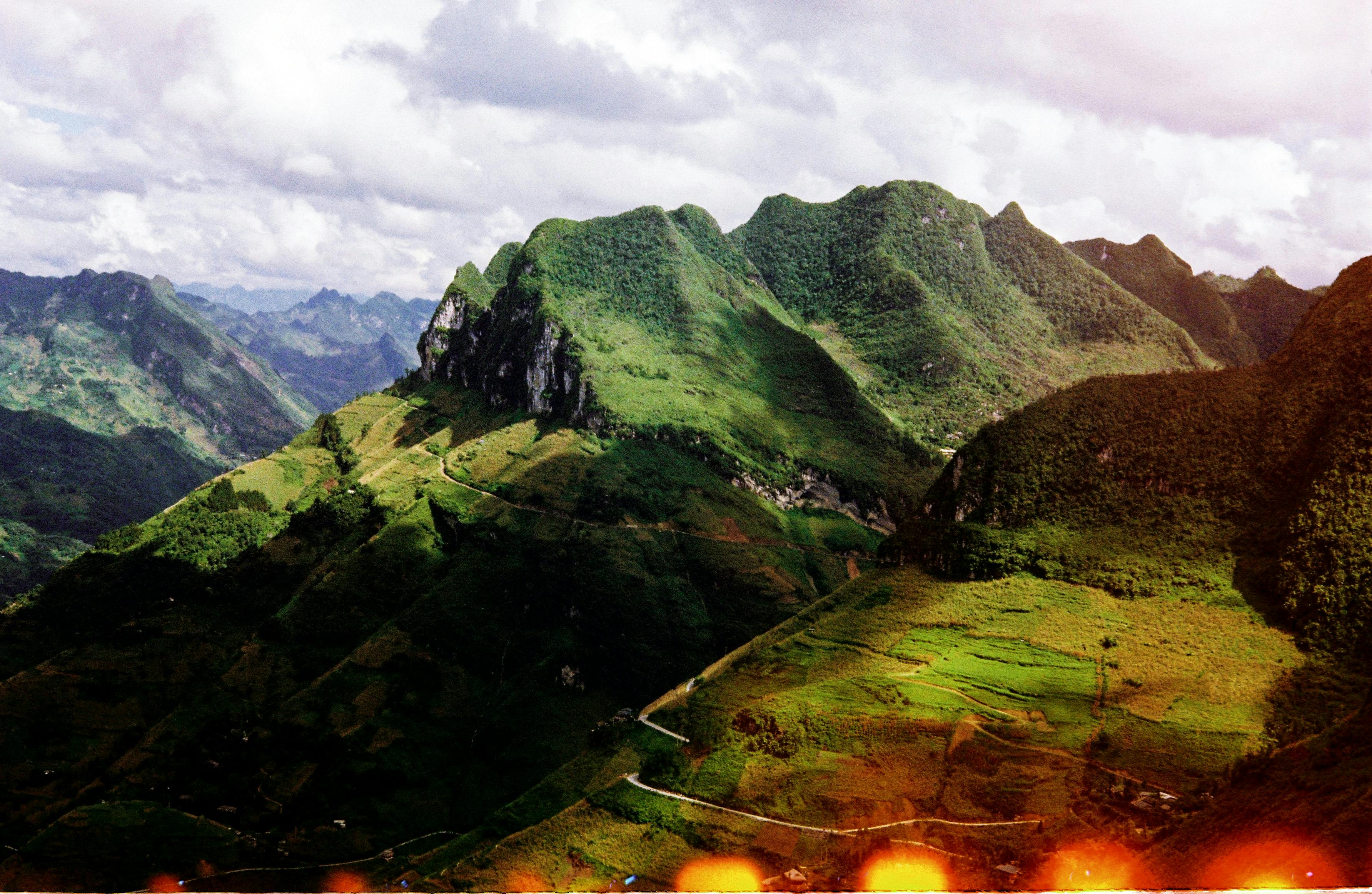 Scenic aerial view of lush green mountains and valleys under a dramatic cloudy sky.