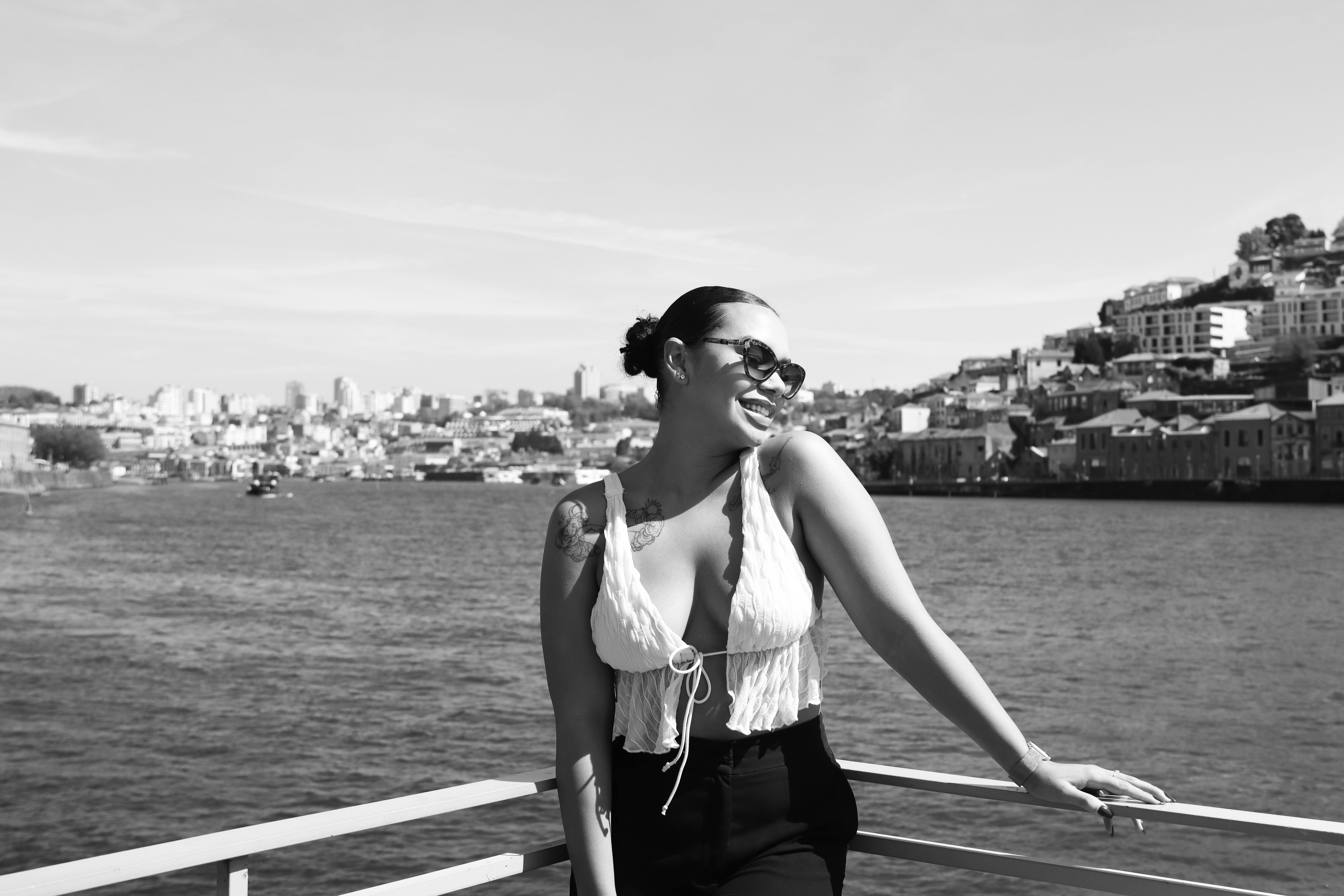 Chic woman in sunglasses smiles by Porto's scenic waterfront, exuding summer vibes.