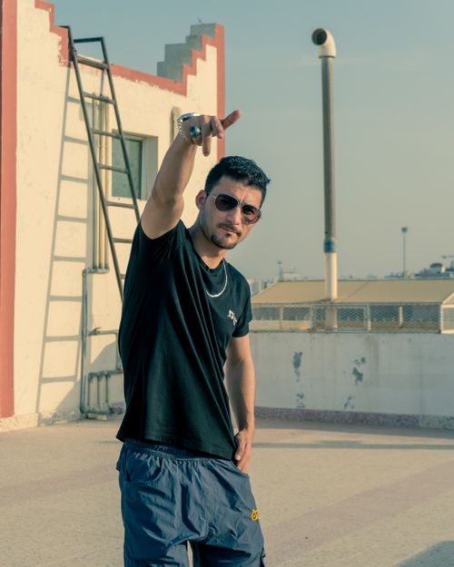 Free Young man in sunglasses and t-shirt poses stylishly on a sunlit rooftop terrace. Stock Photo