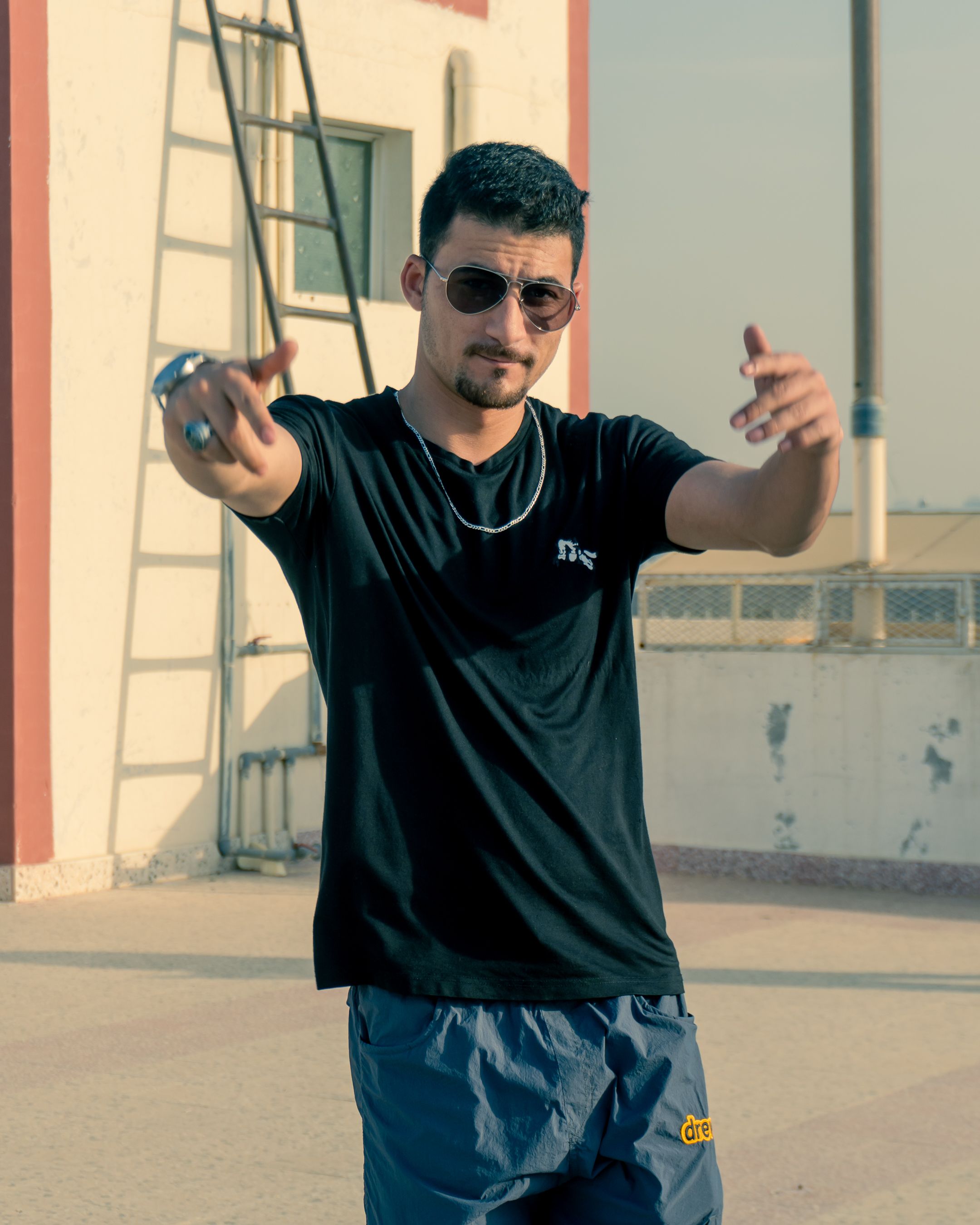 Young man in sunglasses posing confidently on a sunny day, showcasing casual fashion outdoors.