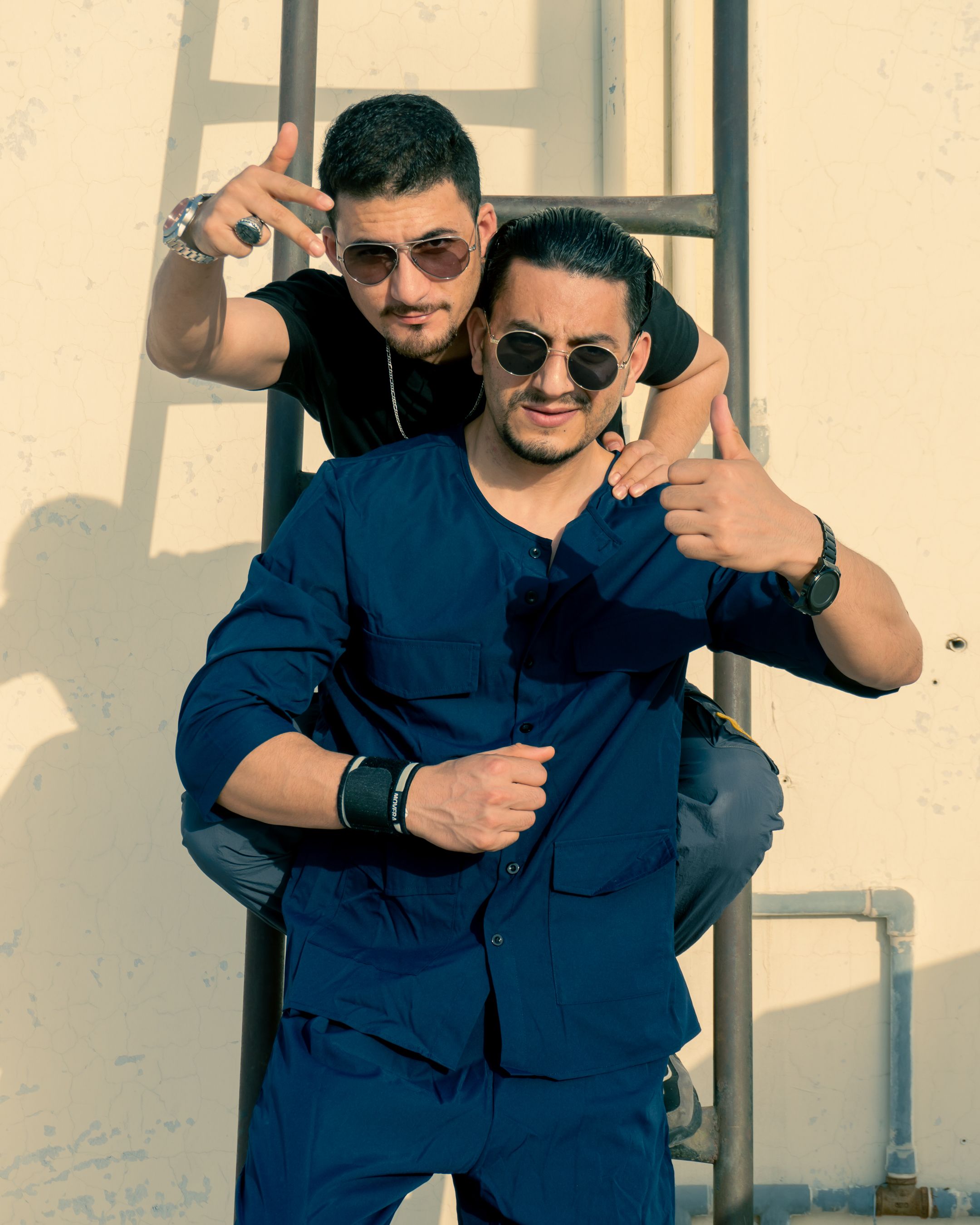 Stylish young men posing creatively on a ladder in sunlight, exuding trendy fashion vibes.