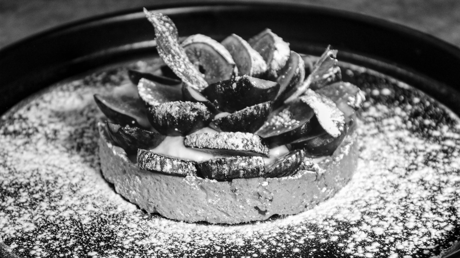 Elegant fig dessert with powdered sugar in black and white on a plate, showcasing gourmet presentation.
