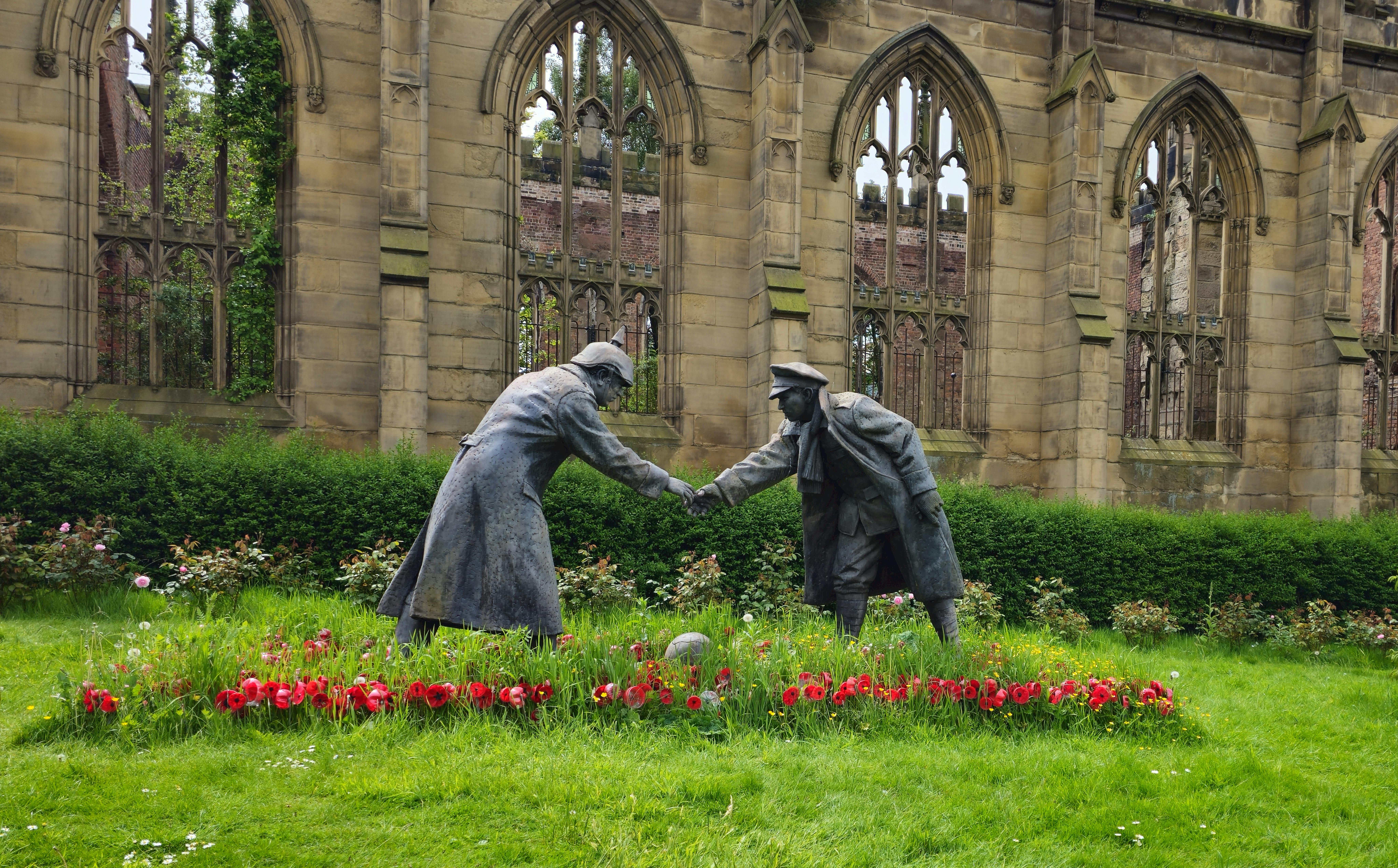 Statues of soldiers shaking hands amidst flowering garden in Liverpool, UK.