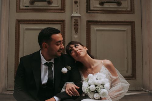 Free Bride and groom embracing affectionately while seated in front of ornate doors. Stock Photo