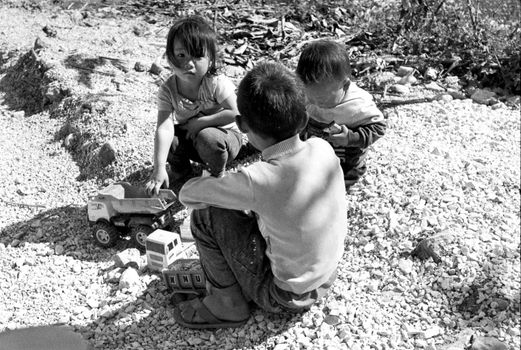 Three children playing with toy cars outdoors, enjoying creative playtime.