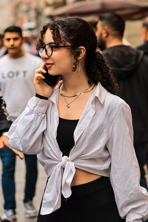 Free Stylish woman with curly hair and glasses talking on the phone outdoors. Stock Photo